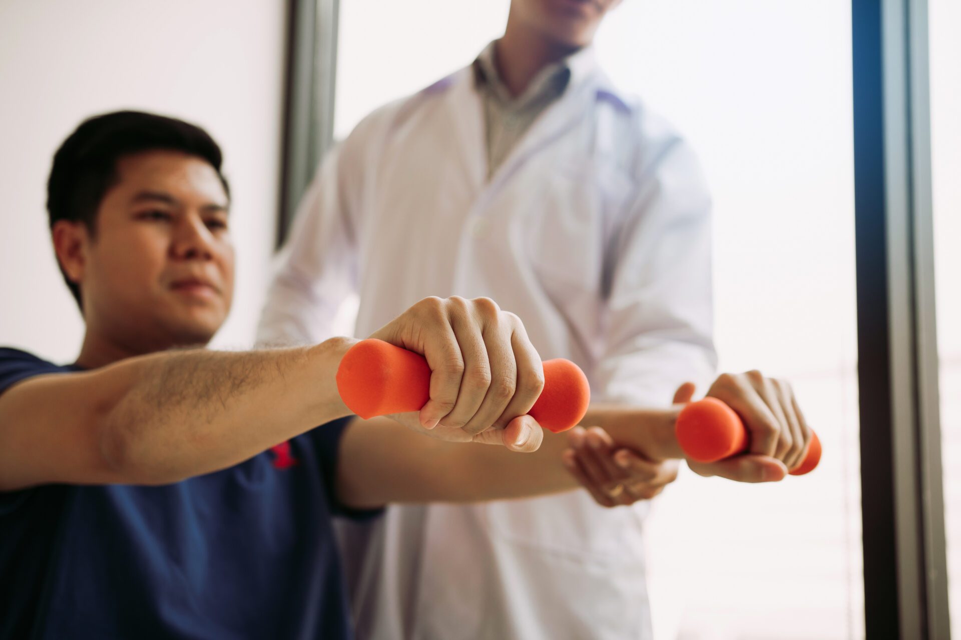 Asian young male physiotherapist helping patient with lifting du A man doing physical exercise